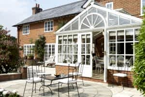 An elegant conservatory attached to a brick house, with outdoor seating on a patio