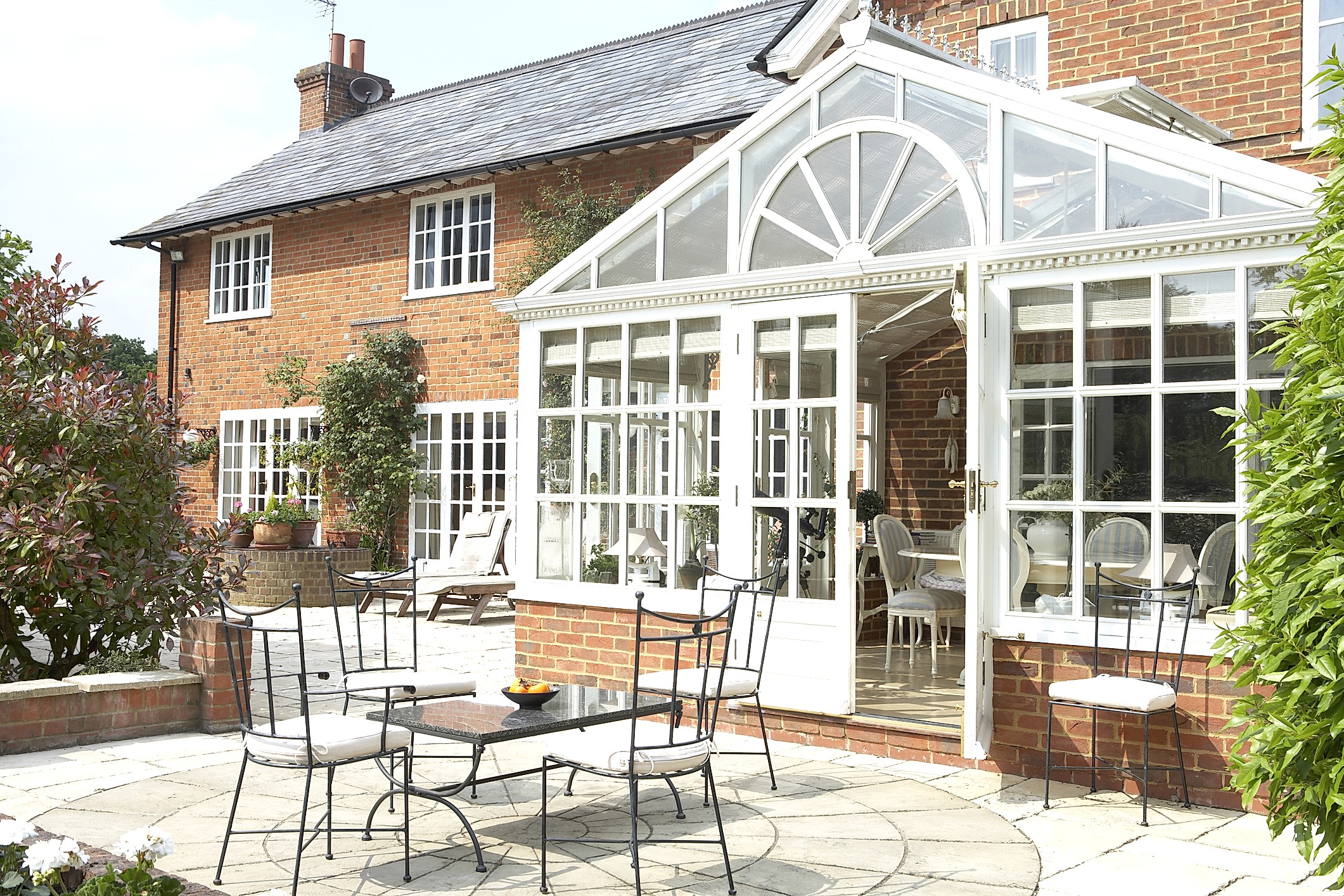 An elegant conservatory attached to a brick house, with outdoor seating on a patio